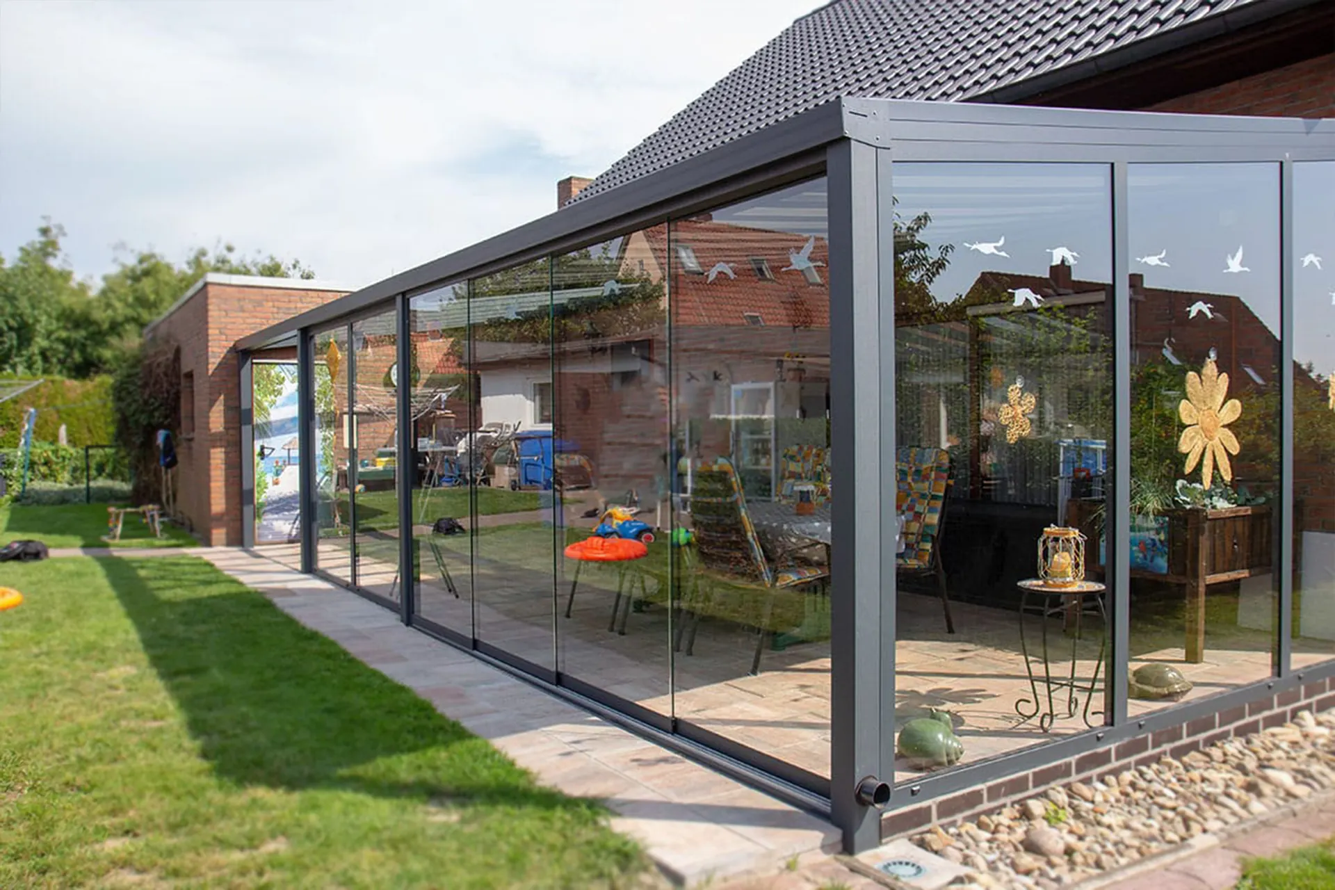 Kaltwintergarten mit Glasschiebewänden und anthrazitfarbenem Rahmen an einem Klinkerhaus