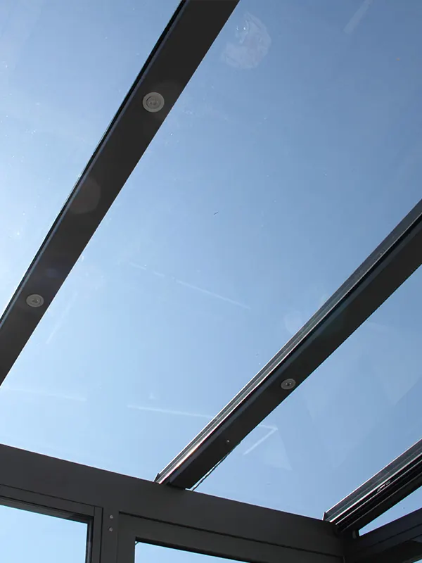 Blick von unten durch ein Glasdach mit anthrazitfarbenen Sparren in den Himmel