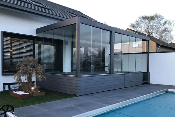 Verglaster Kaltwintergarten mit anthrazitfarbenem Rahmen neben einem Pool